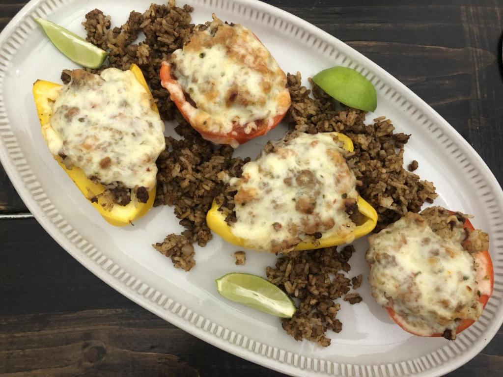 Vegetarian stuffed peppers sit atop a dining table next to chips and salsa.
