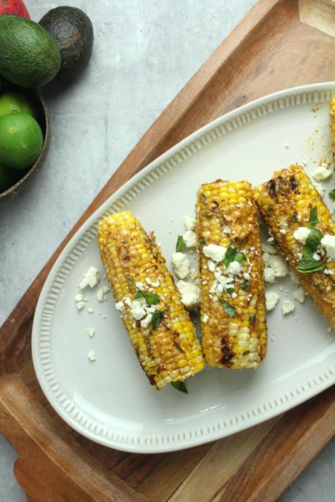 Mexican street corn is served on a platter alongside limes, avocado, and mango.