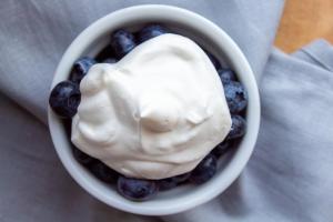 Whipped cream is plopped on top of a bowl of blueberries.