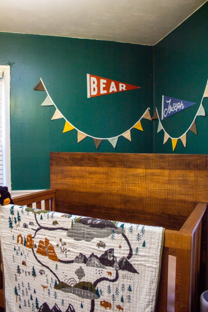 A national park theme nursery shows a crib with quilt and banners and pennants behind it.