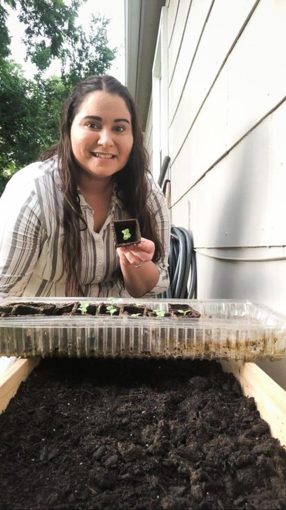 A woman is holding seedlings over a garden bed as she learns how to layer a raised garden bed.