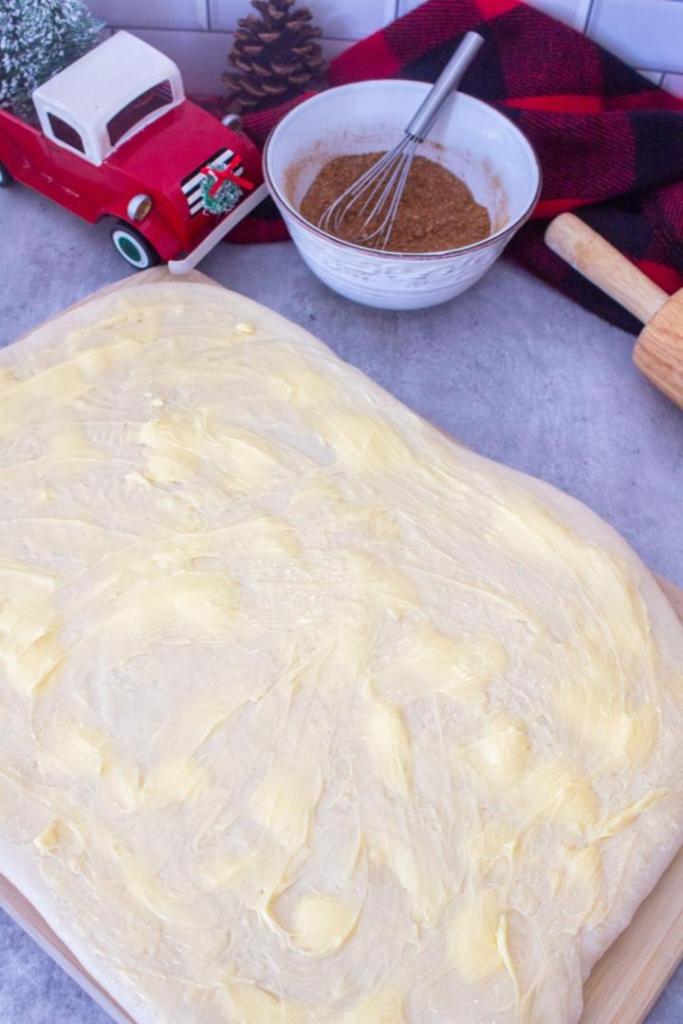 Butter is spread on top of rolled out dough to make fluffy cinnamon rolls.
