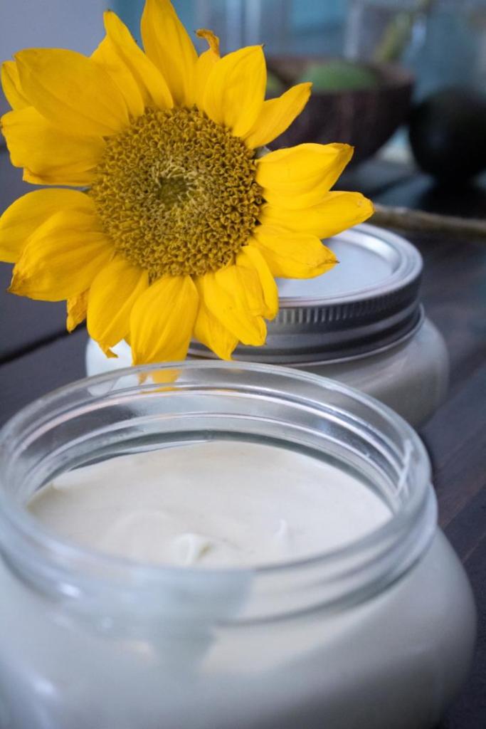 DIY whipped body butter recipe is finished and in a jar with a sunflower draped over it.