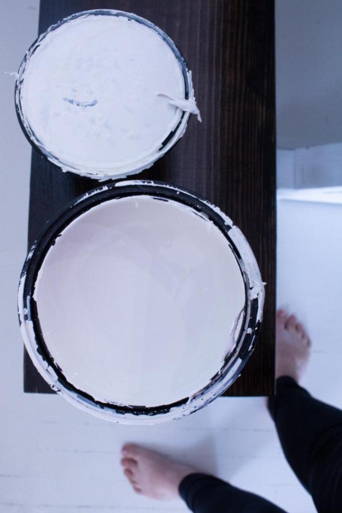 A woman looks down on a bench with a can of opened paint.