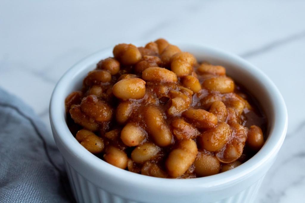 Baked beans are served in a white bowl on a countertop.