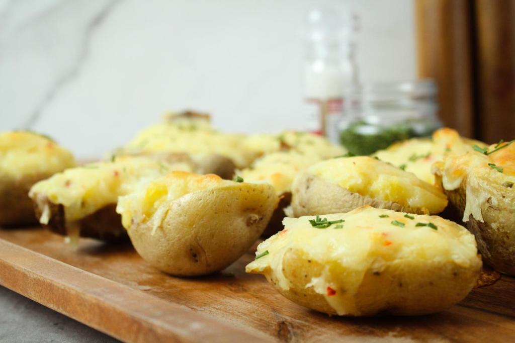 Easy twice baked potatoes are served alongside one another on a wood tray. 