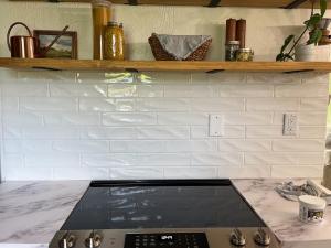 A DIY subway tile backsplash is shown with a glossy sheen above a range and below open shelving.