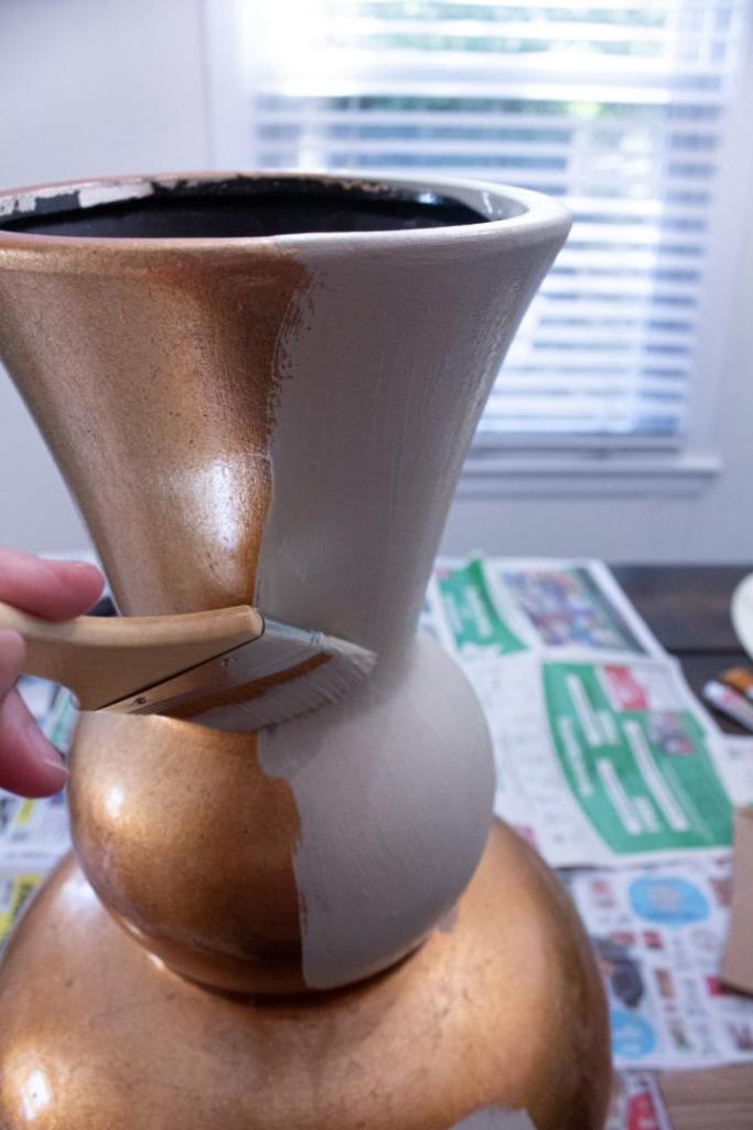 A gold vase is being painted a light beige color.
