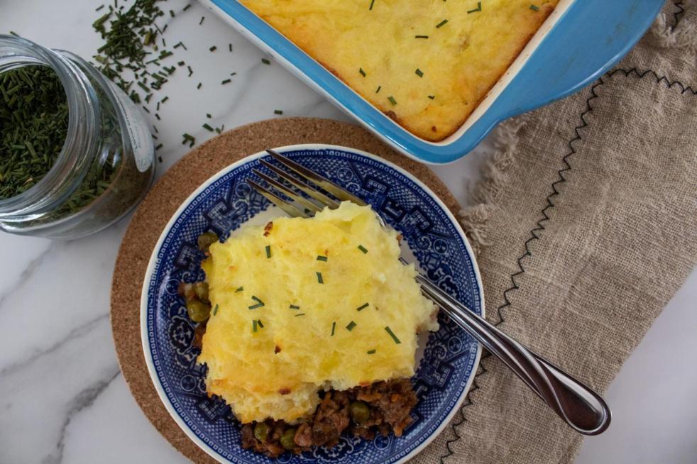Impossible meat shepherd's pie is dished out on a blue saucers next to a jar of spilled chives as a vegetarian meal prep idea.
