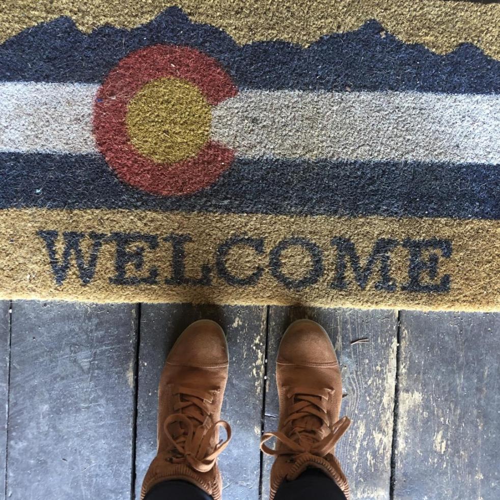 A woman poses in her hiking boots beside a welcome mat in a Colorado cabin.