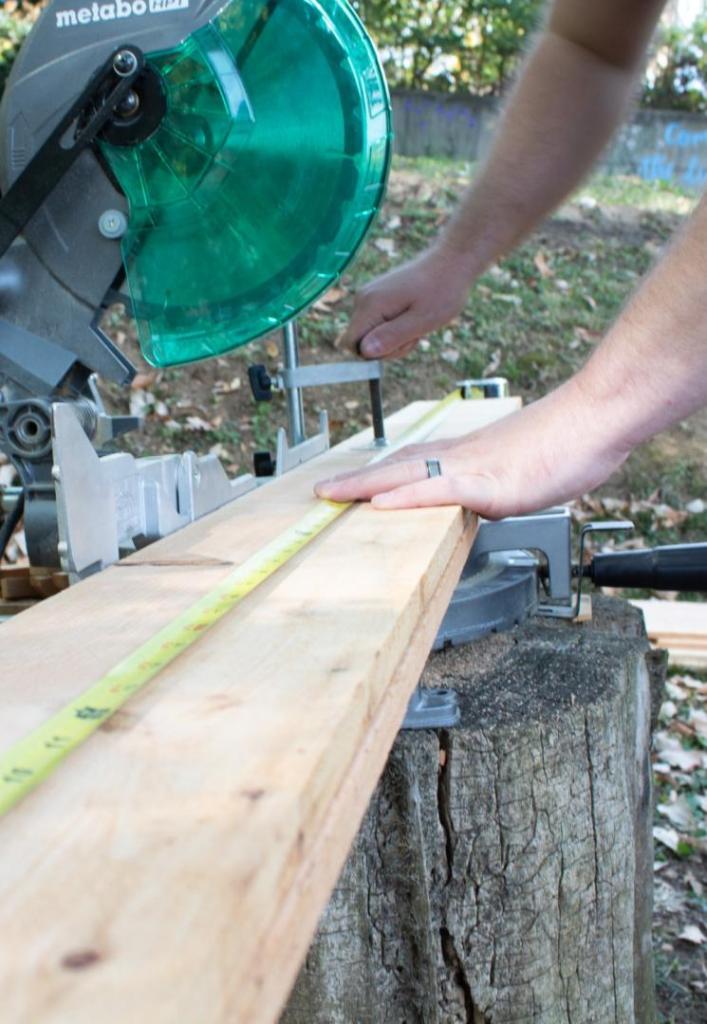 A man cuts a fence picket in half for two shorter sides of a garden bed.