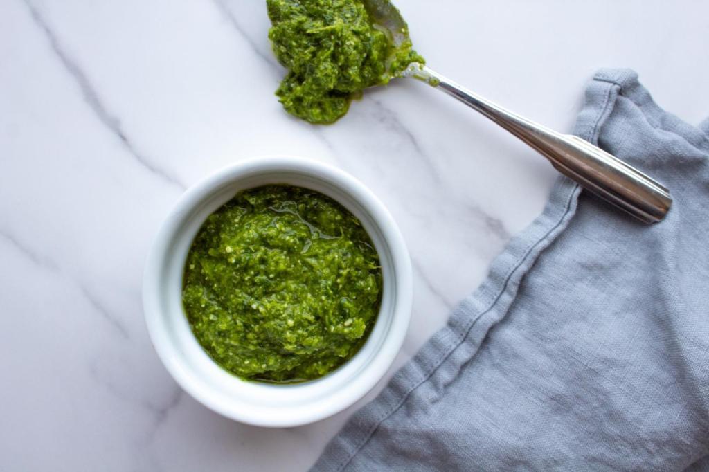 Garlic scape pesto is in a ramekin and also in a spoon on a counter.