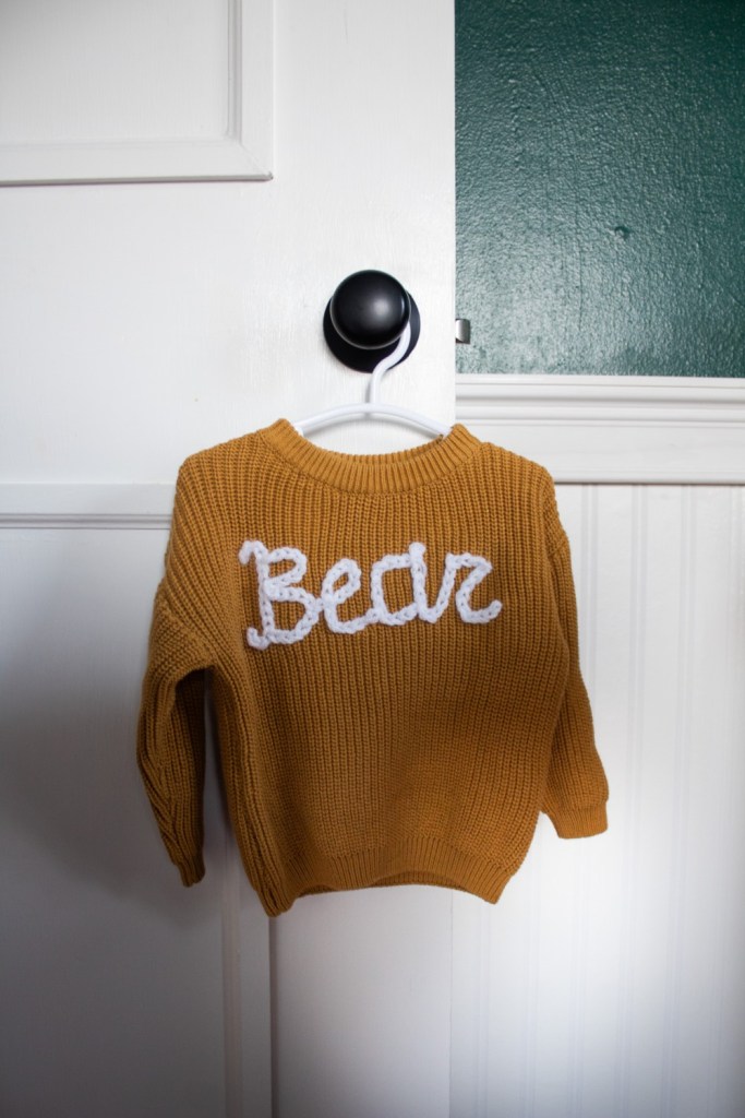 A sweater reads "Bear" on it and hangs in a doorway.