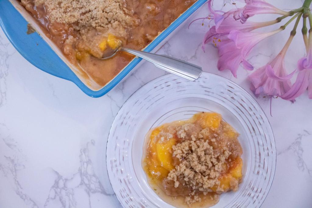 A peach crumble recipe is served on a saucer next to pink lilies.