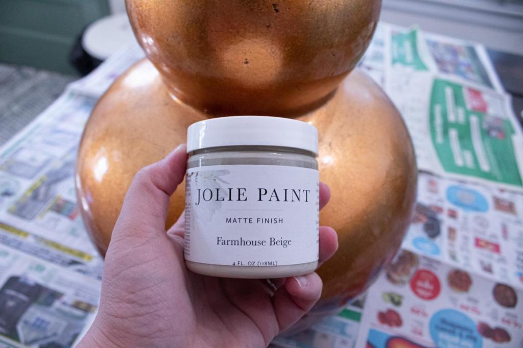 A DIY textured vase is about to be made using a beige paint pictured alongside a gaudy gold vase.