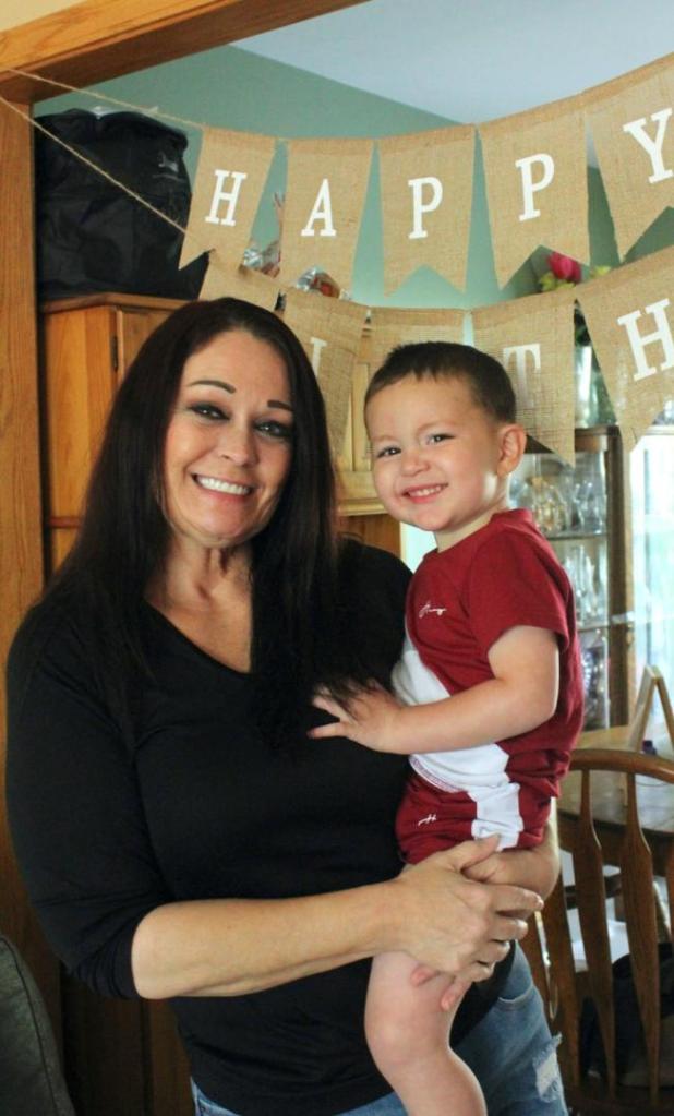 A woman holds her grandchild under a banner at a home birthday party.