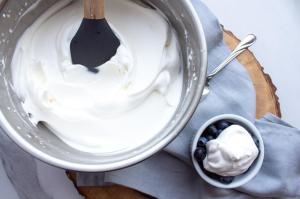 A bowl of whipped cream is placed next to blueberries after learning how to make homemade whipped cream with heavy cream.