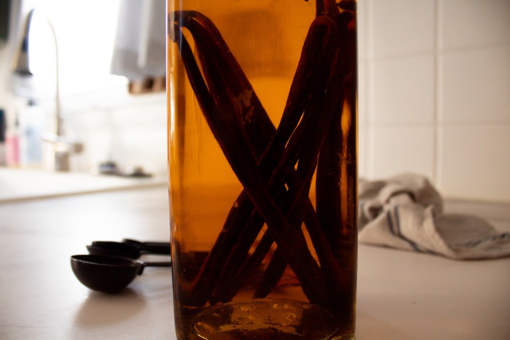 A vanilla extract recipe with vodka is sitting on a countertop with measuring spoons nearby.