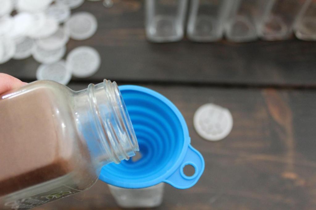A spice jar is being poured into another jar through a funnel.