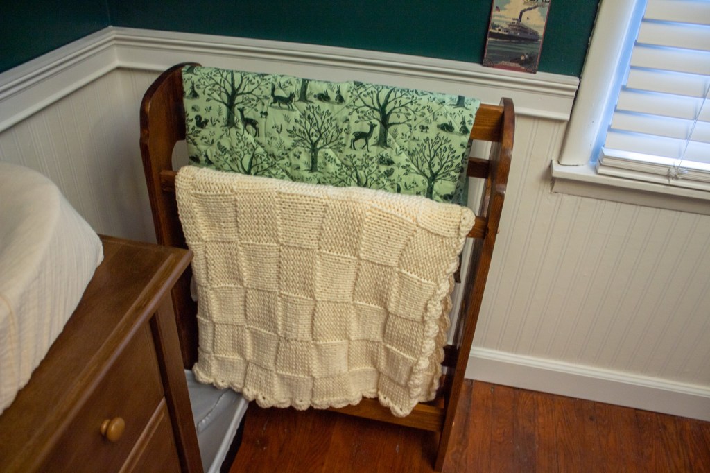 A woodland animals quilt and crocheted Afghan are pictured on a quilt stand.