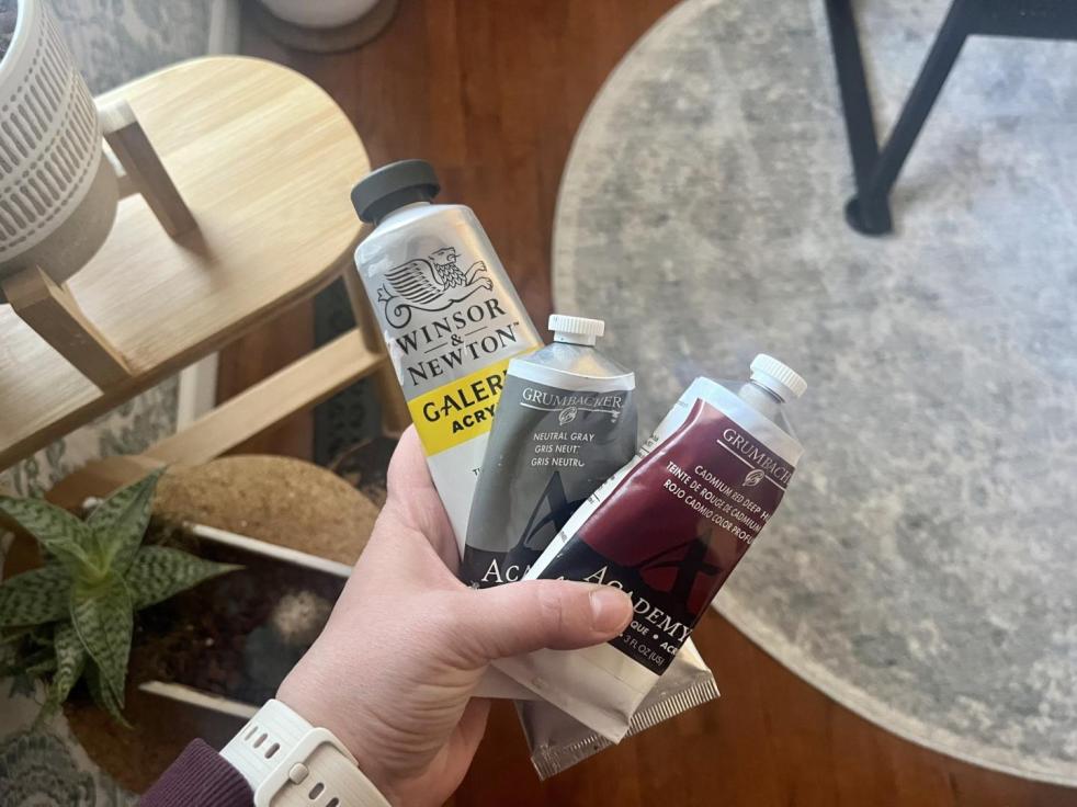 A woman holds tubes of paint in her hand.