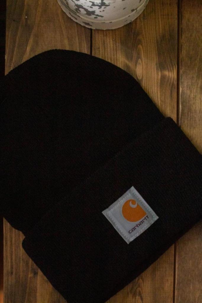 A Carhartt beanie lays on a side table as part of a stocking stuffer idea for adults.