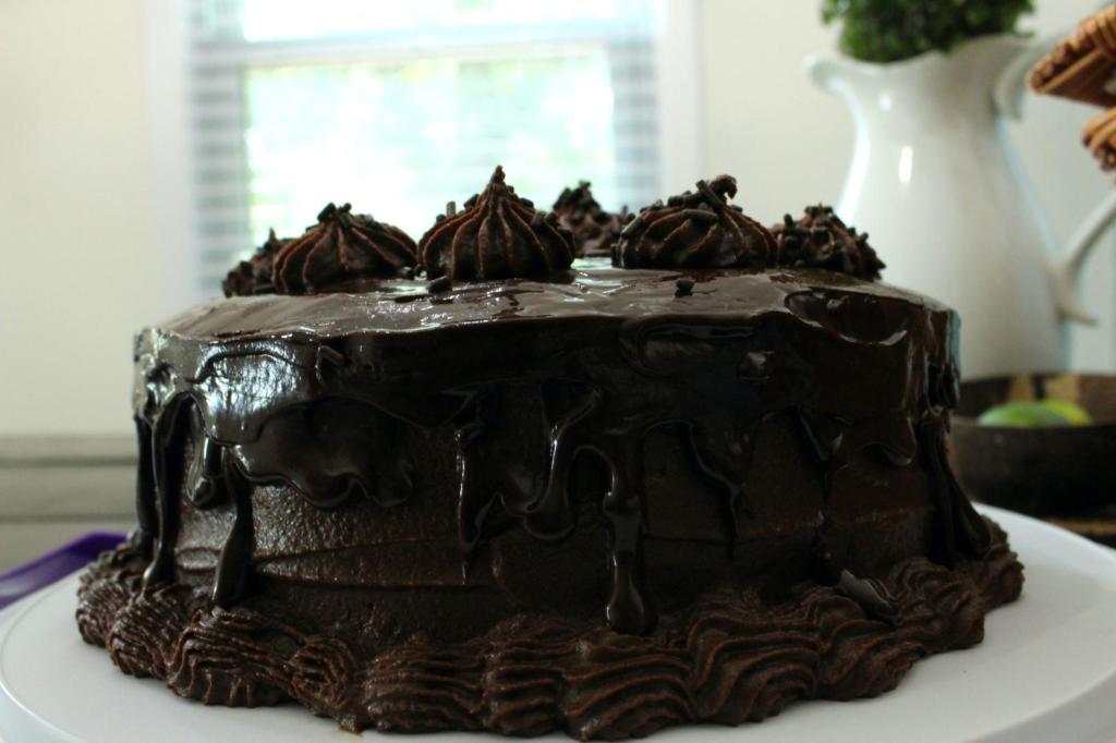 A side view of a rich chocolate birthday cake sits on a table.