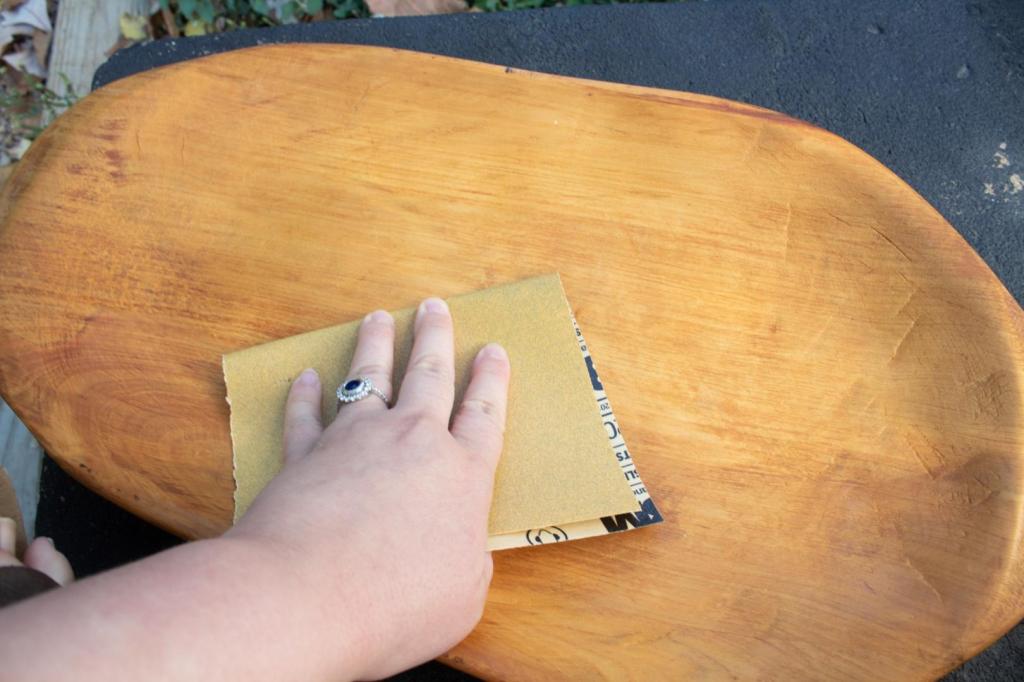 A woman begins sanding a wooden platter using 220-grit sandpaper.