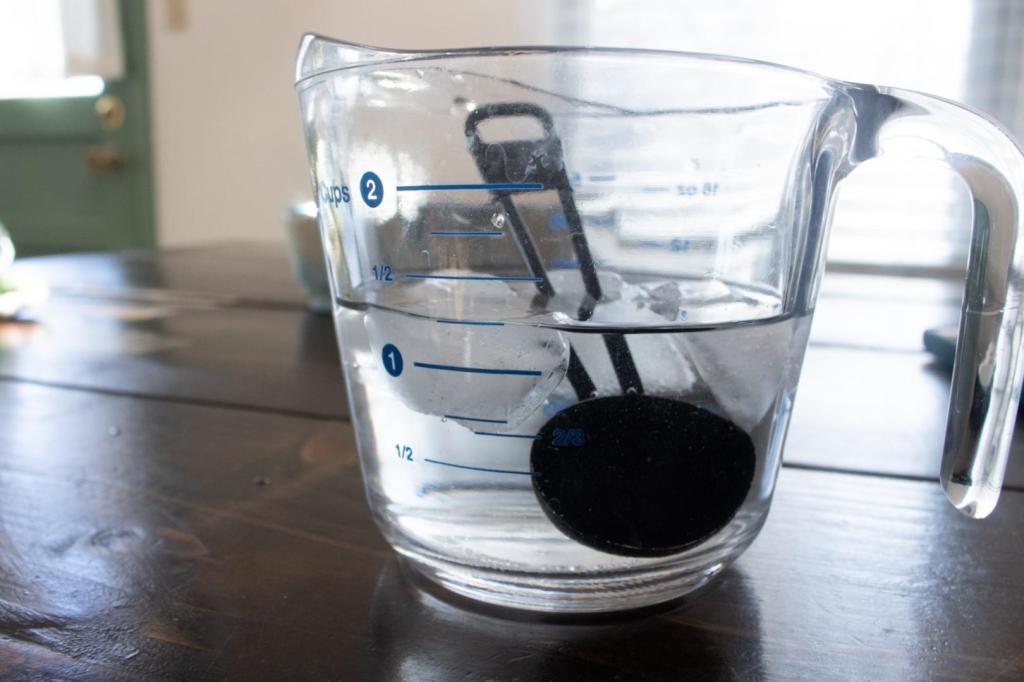 A glass measuring cup has water and ice in it, along with a measuring spoon.