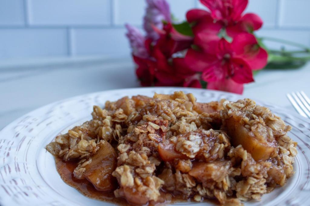 Crockpot Apple Crisp is served on a small plate with right red flowers behind it.