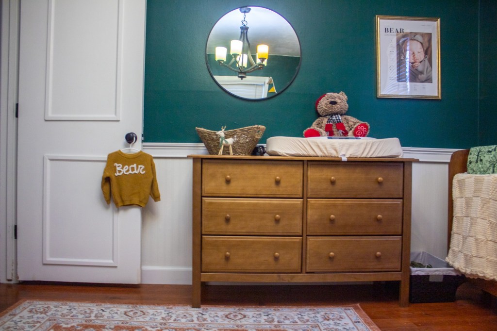 A nursery with green walls, rust colored rugs, and chestnut woods exudes a national park theme.