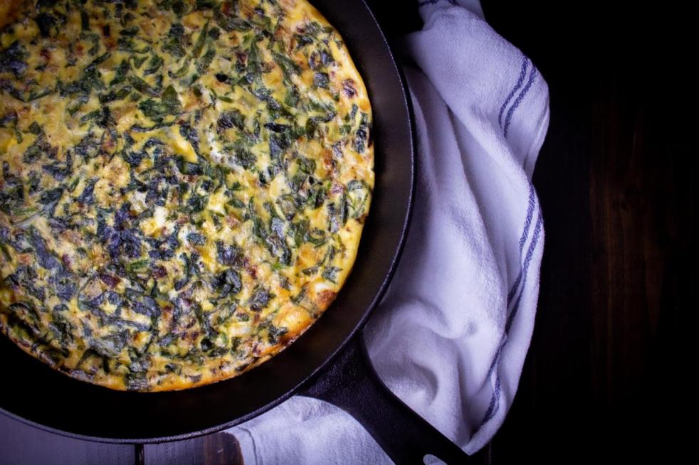 A spinach mozzarella crustless quiche sits in a cast iron skillet on a tabletop next to a towel.