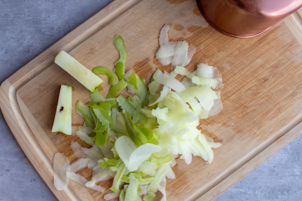 Apple scraps are scattered about on a wooden cutting board.