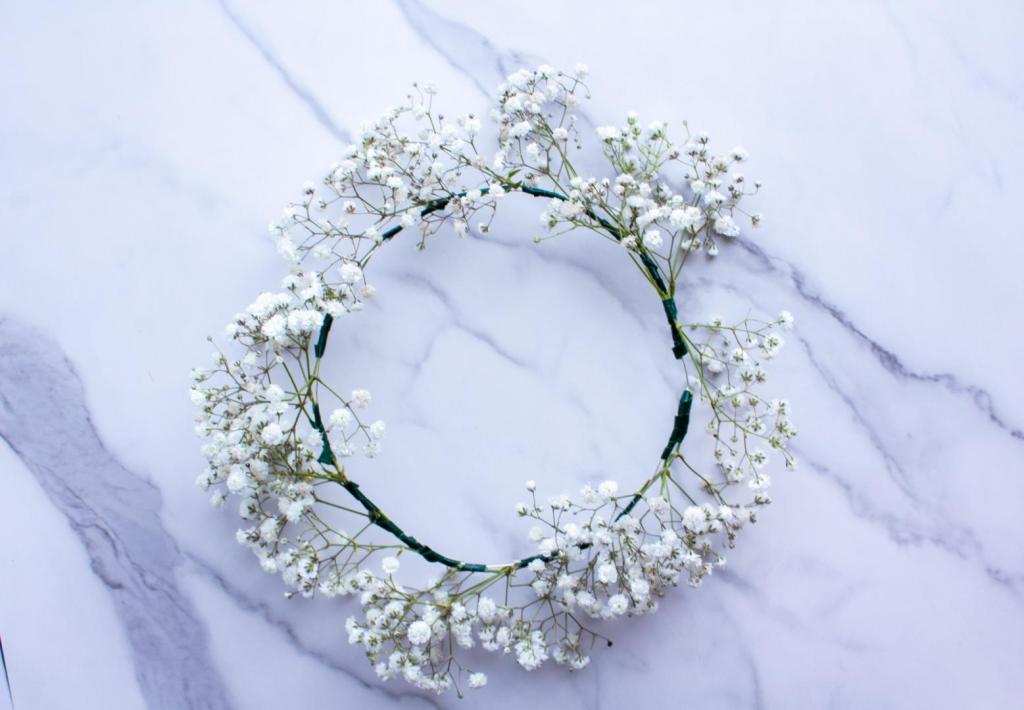 A baby's breath floral crown is finished and lays on a marble countertop.
