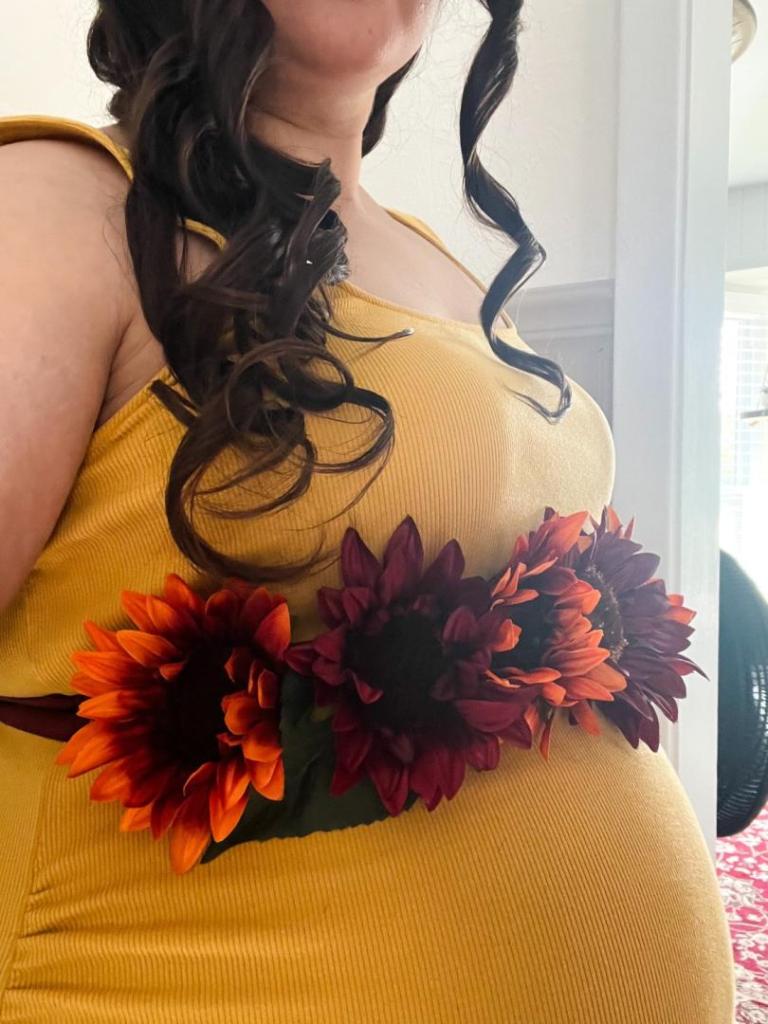 A woman shows off her burgundy sunflower belt for a baby shower.