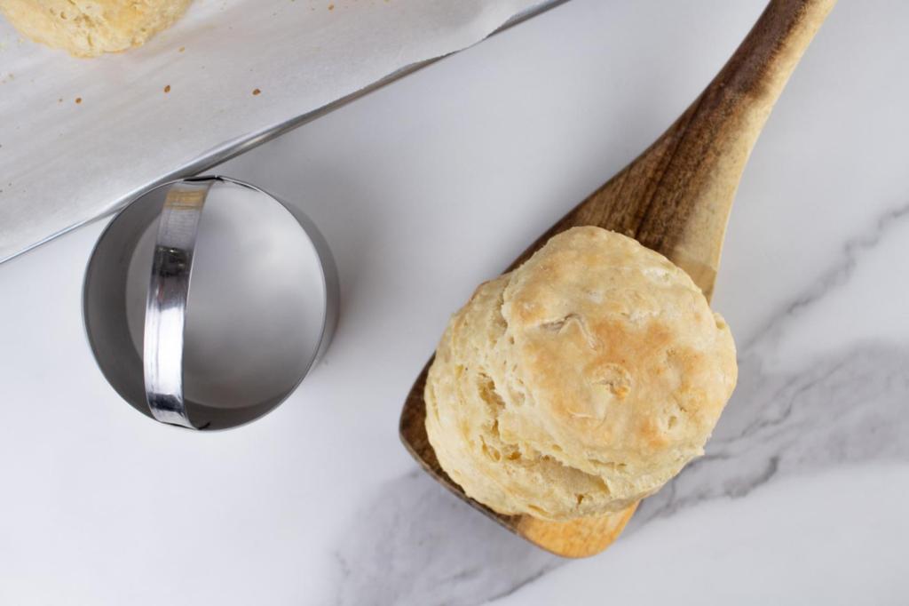 A biscuit sits on a countertop with a spatula and a biscuit cutter.