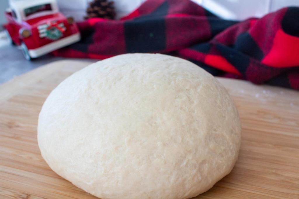 The ball of dough is smooth and elastic after being kneaded on a wood cutting board.