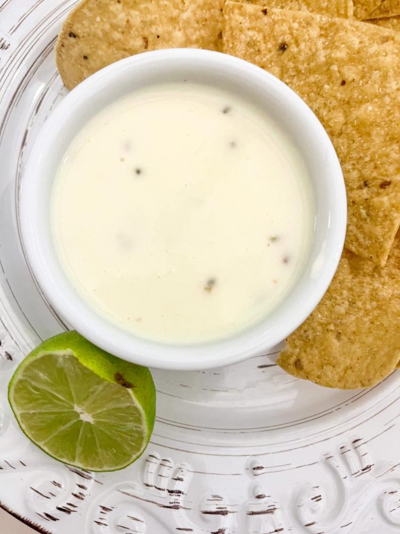 easy homemade queso recipe is shown with chips and a lime.