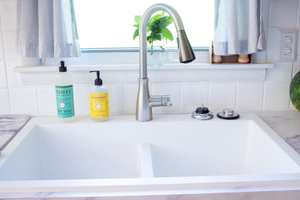 A white farmhouse sink is shown front and center in a post about how to clean a quartz sink.
