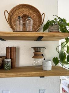 Several kitchen items are shown on open shelving in a cottage kitchen, including a pour over coffee maker, plant, pepper & salt mill, baskets, and more.