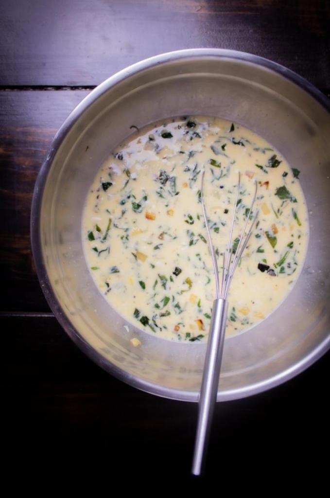 An egg mixture is whisked into a metal mixing bowl.