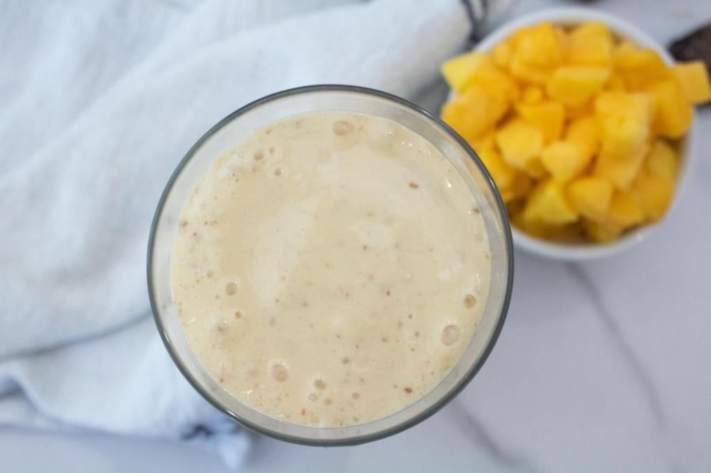 A tropical smoothie has been blended up and sits next to mango on a counter.