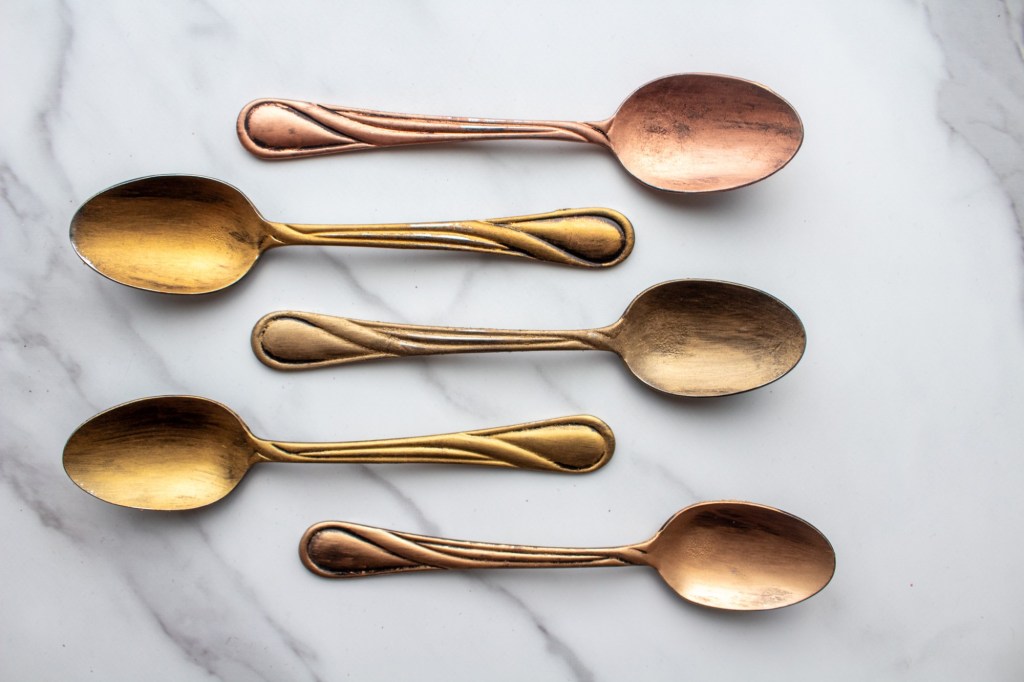 Rub n buff golds are painted on spoons and arranged in a row.