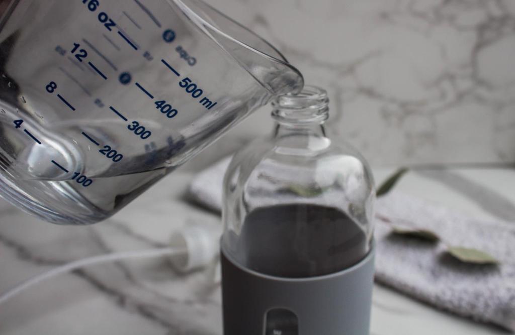 A woman pours vinegar into a spray bottle.