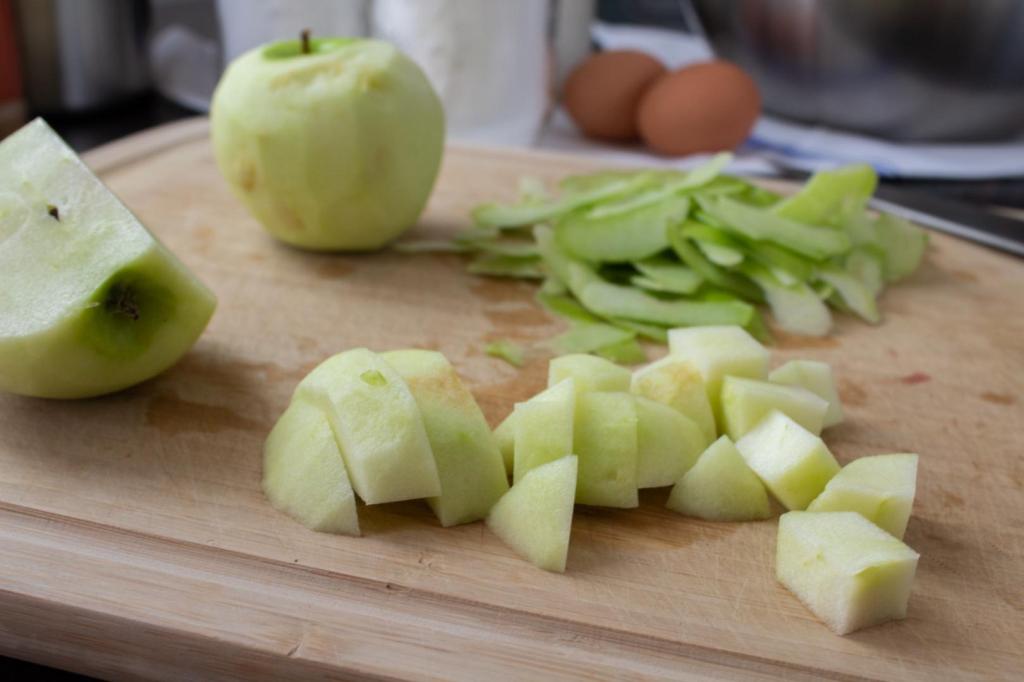 Apples are peeled and chopped on a cutting board.