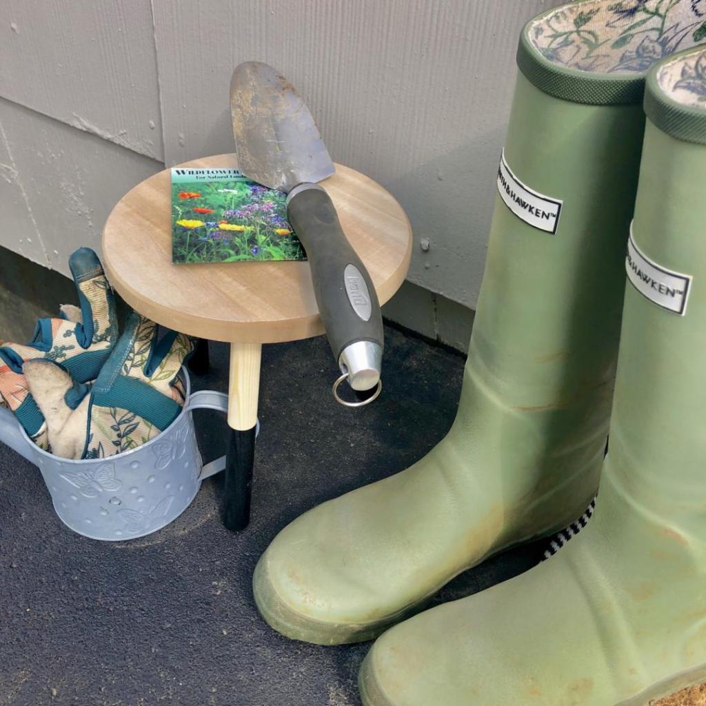 Gardening boots, a shovel, and gloves sit outside on a porch.