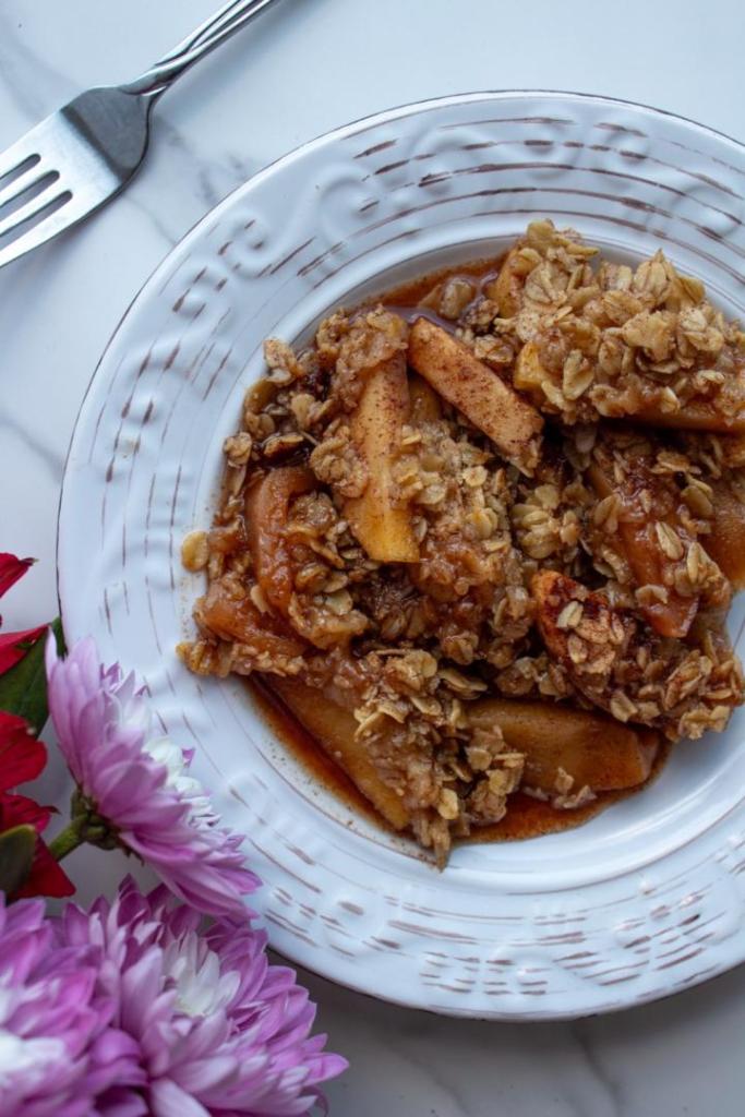 Crockpot Apple Crisp is served on a plate with its oats, cinnamon, and apples piled high.