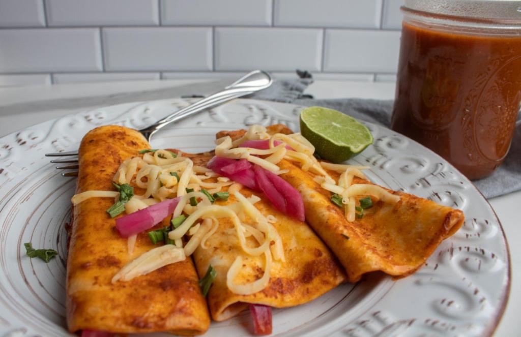 Vibrant enchiladas have enchilada sauce and garnishes added to its plate.