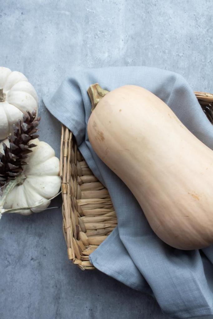 Butternut squash is laid into a basket and presented next to pumpkins on a countertop.