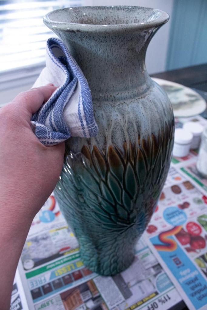 A woman wipes down a blue vase with a cloth.